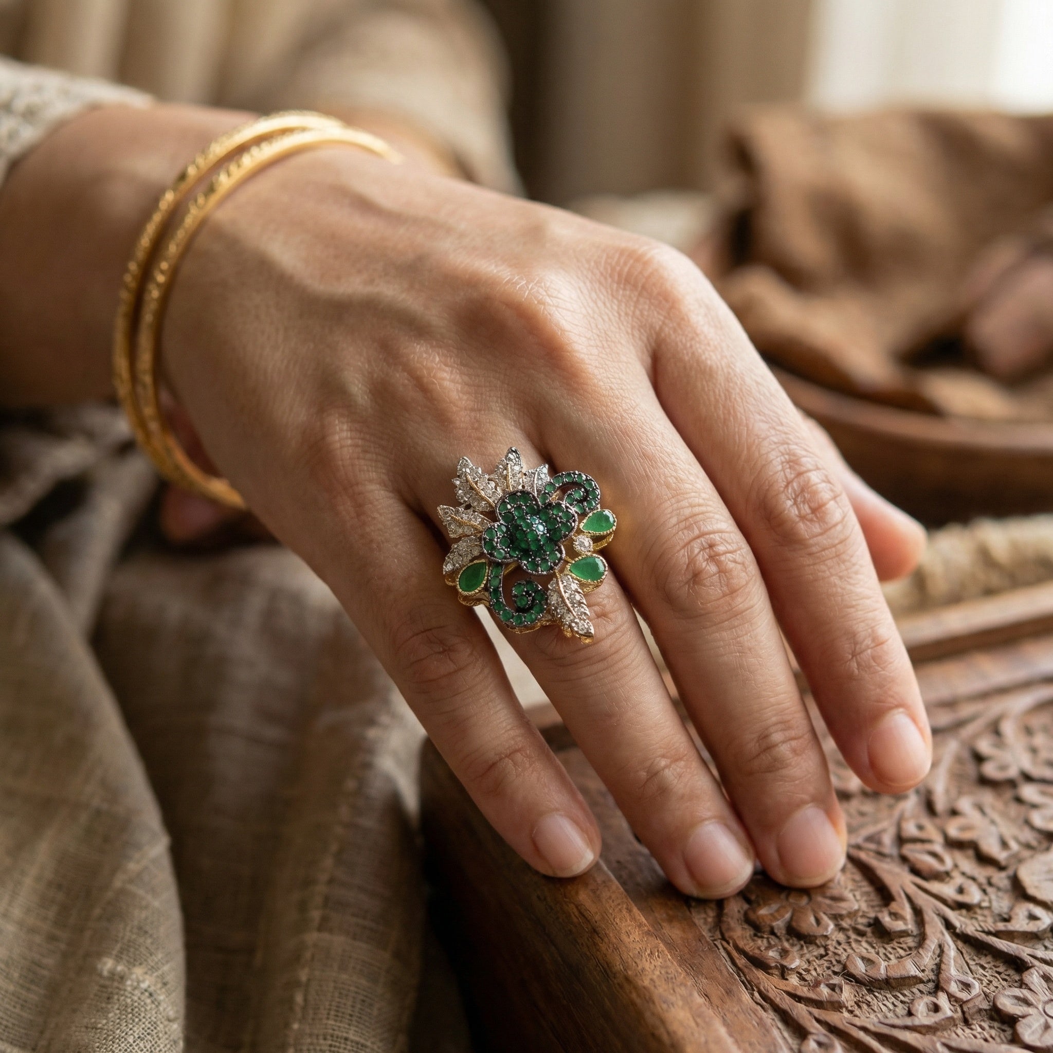 Hand wearing a decorative ring with green gemstones on a textured surface
