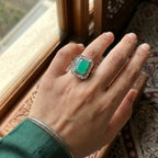 Hand wearing a ring with a green gemstone in front of a window