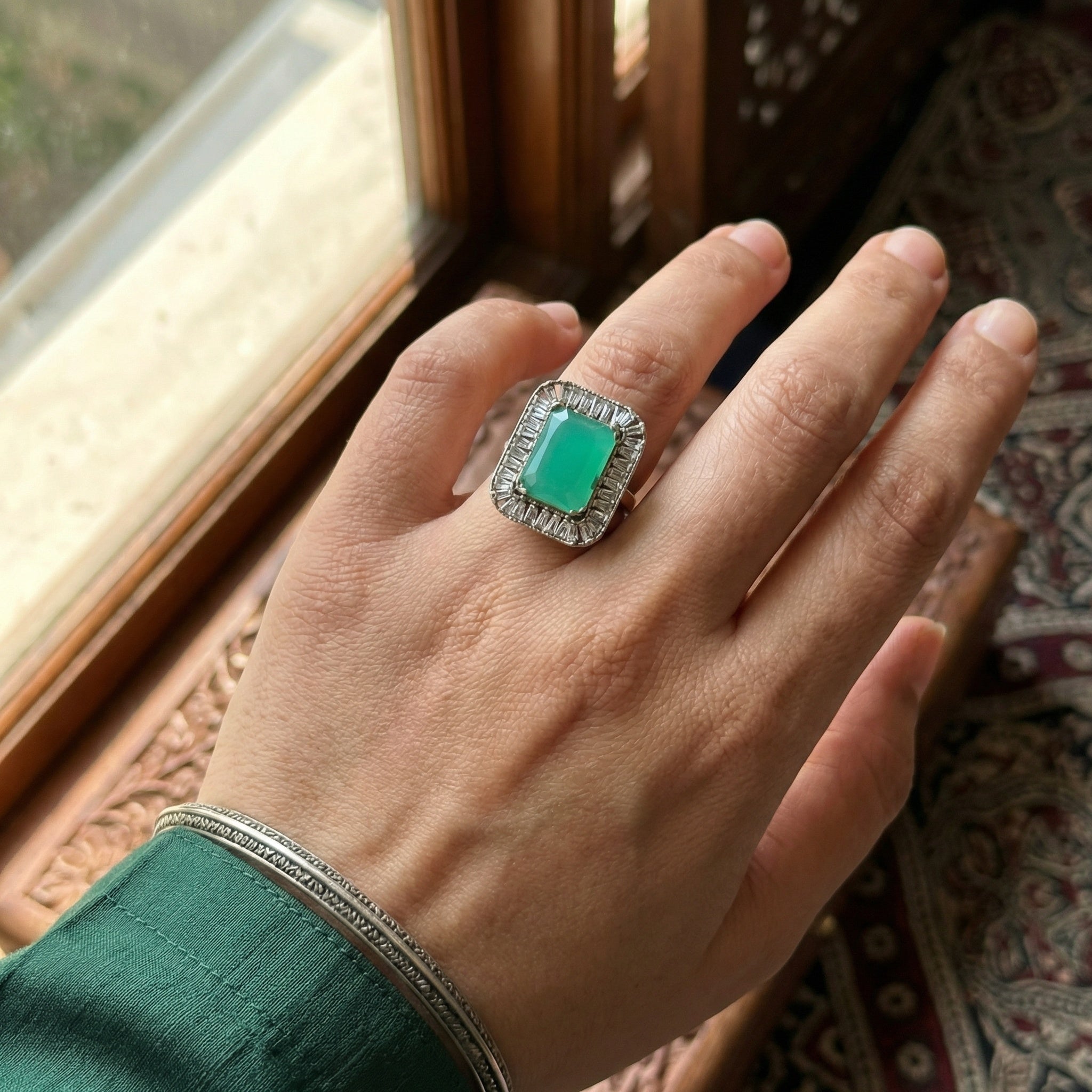 Hand wearing a ring with a green gemstone in front of a window