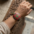 Hand wearing a decorative pink bracelet with turquoise stones against a wooden background