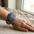 Hand wearing a colorful bracelet with a floral design, sitting on a surface with a window in the background.