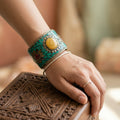 Hand wearing a decorative turquoise bracelet with a yellow stone on a wooden surface.