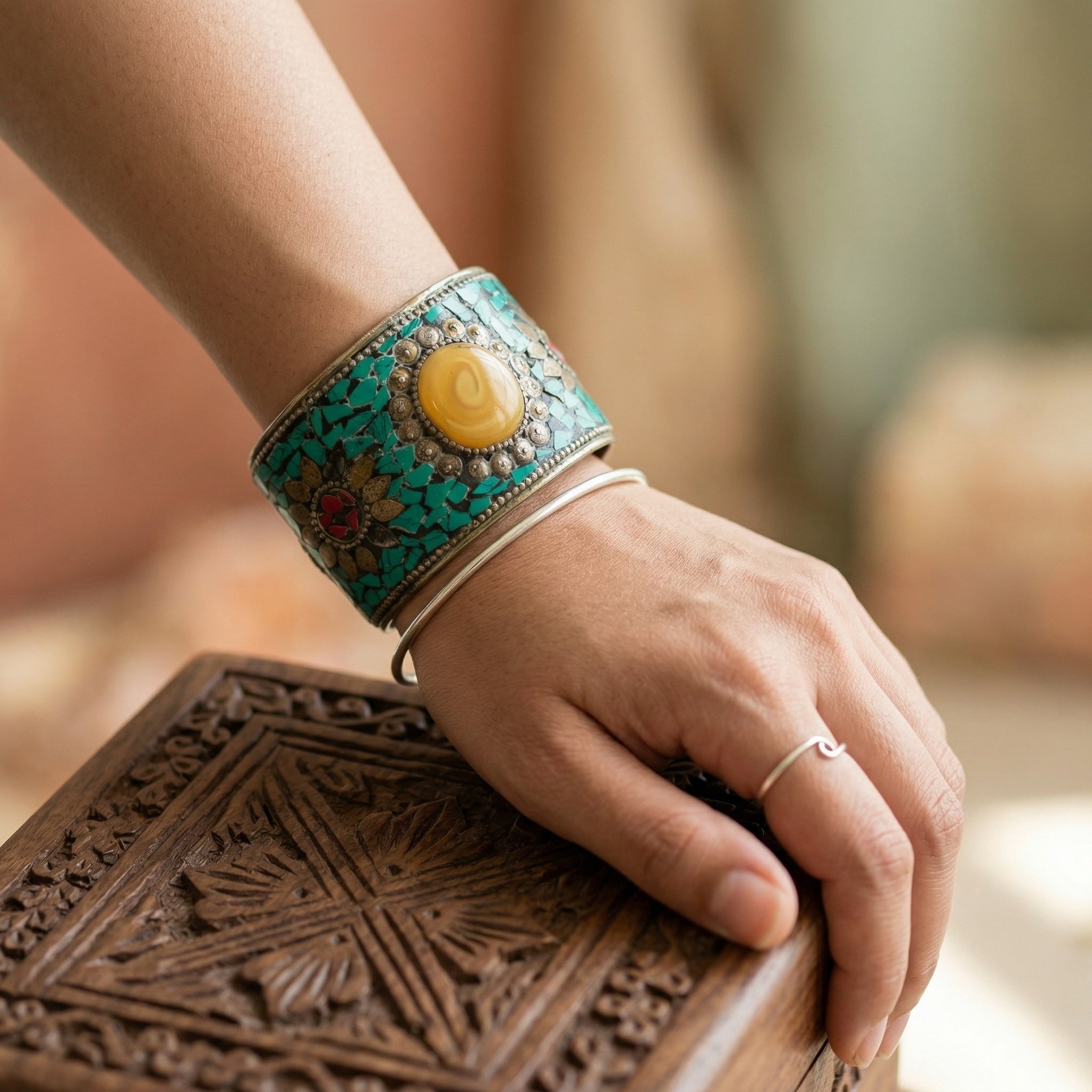 Hand wearing a decorative turquoise bracelet with a yellow stone on a wooden surface.