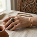 Hand wearing a gold ring with gemstones on a textured surface