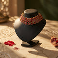Red and gold necklace/choker on a black mannequin bust with decorative elements on a textured marble surface.