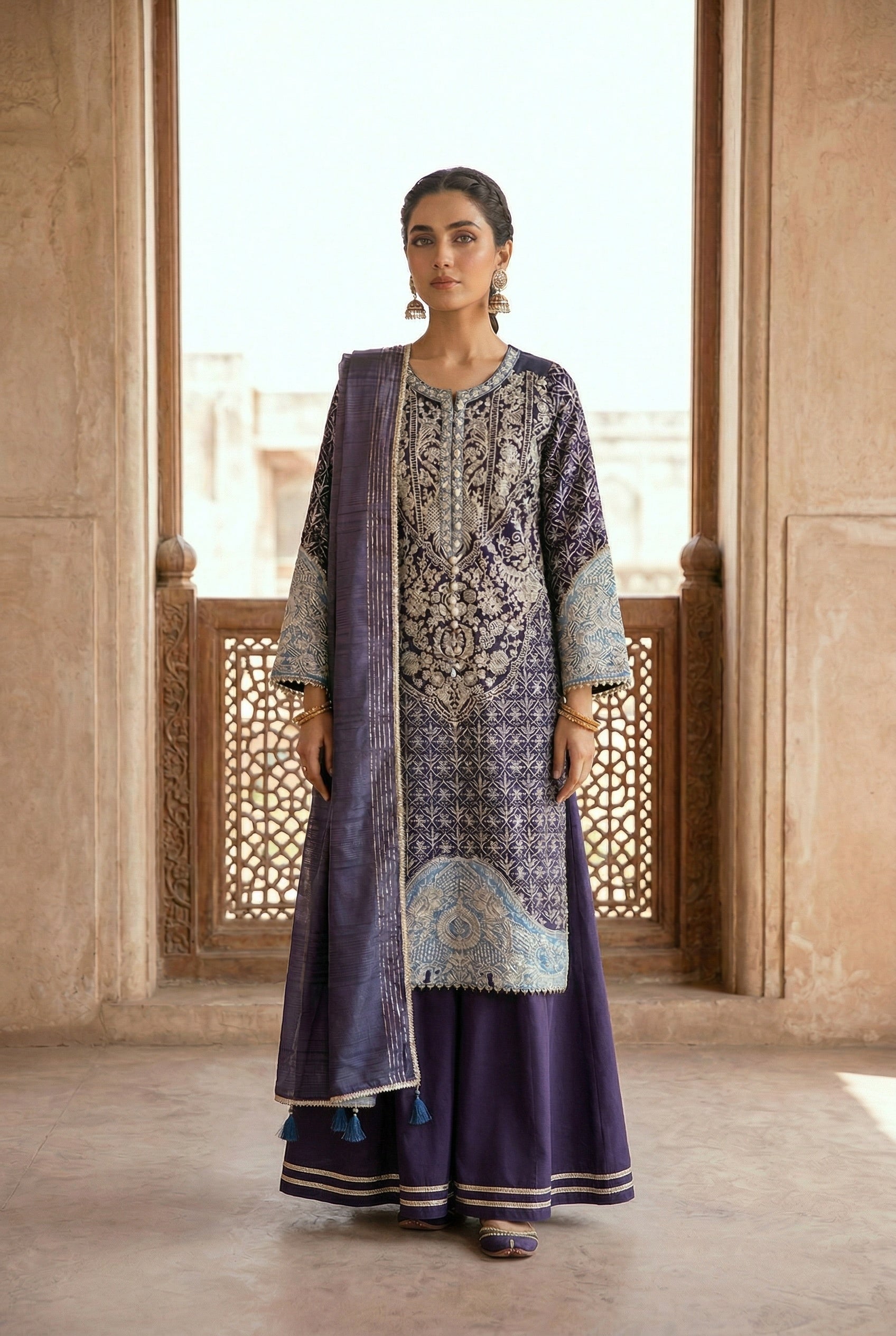 Woman wearing a traditional outfit with intricate patterns in a sunlit room.