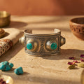 Bronze bracelet with turquoise stones on a rustic surface with bowls and stones.