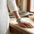 Person wearing a silver cuff with turquoise stones on a marble surface.