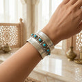 Silver cuff with turquoise stones on a wrist, with a blurred indoor background with marble counters.