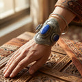 Hand wearing an silver cuff with blue stones on a wooden engraved surface.