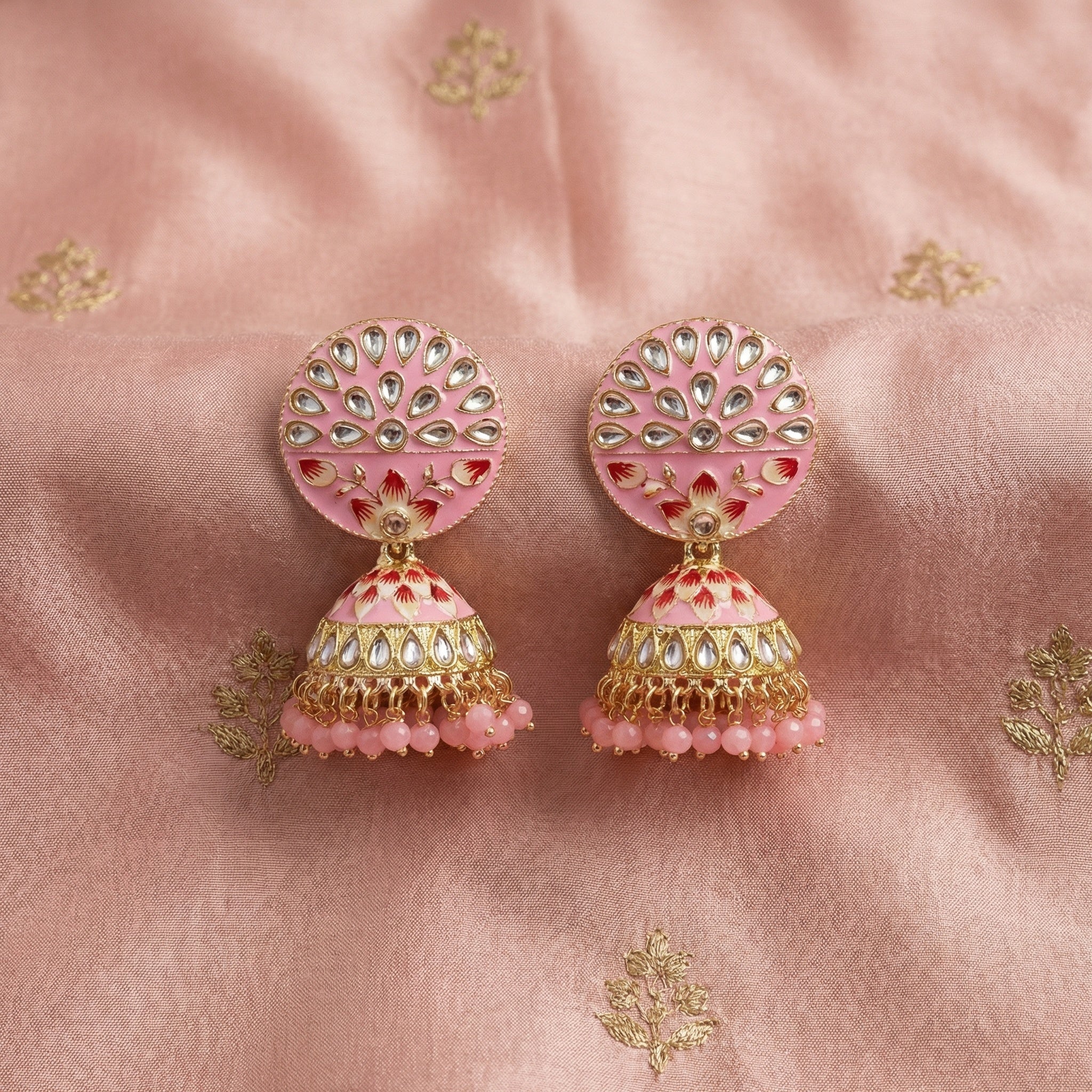 Pair of pink and gold earrings on a pink fabric background