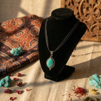 Turquoise necklace on a black velvet stand with decorative stones and fabric in the background