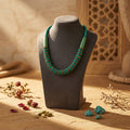 Turquoise beaded necklace on a gray/black mannequin bust with dried flowers on a stone surface.