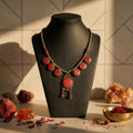 Necklace with red stones on a black mannequin bust against a tiled wall.
