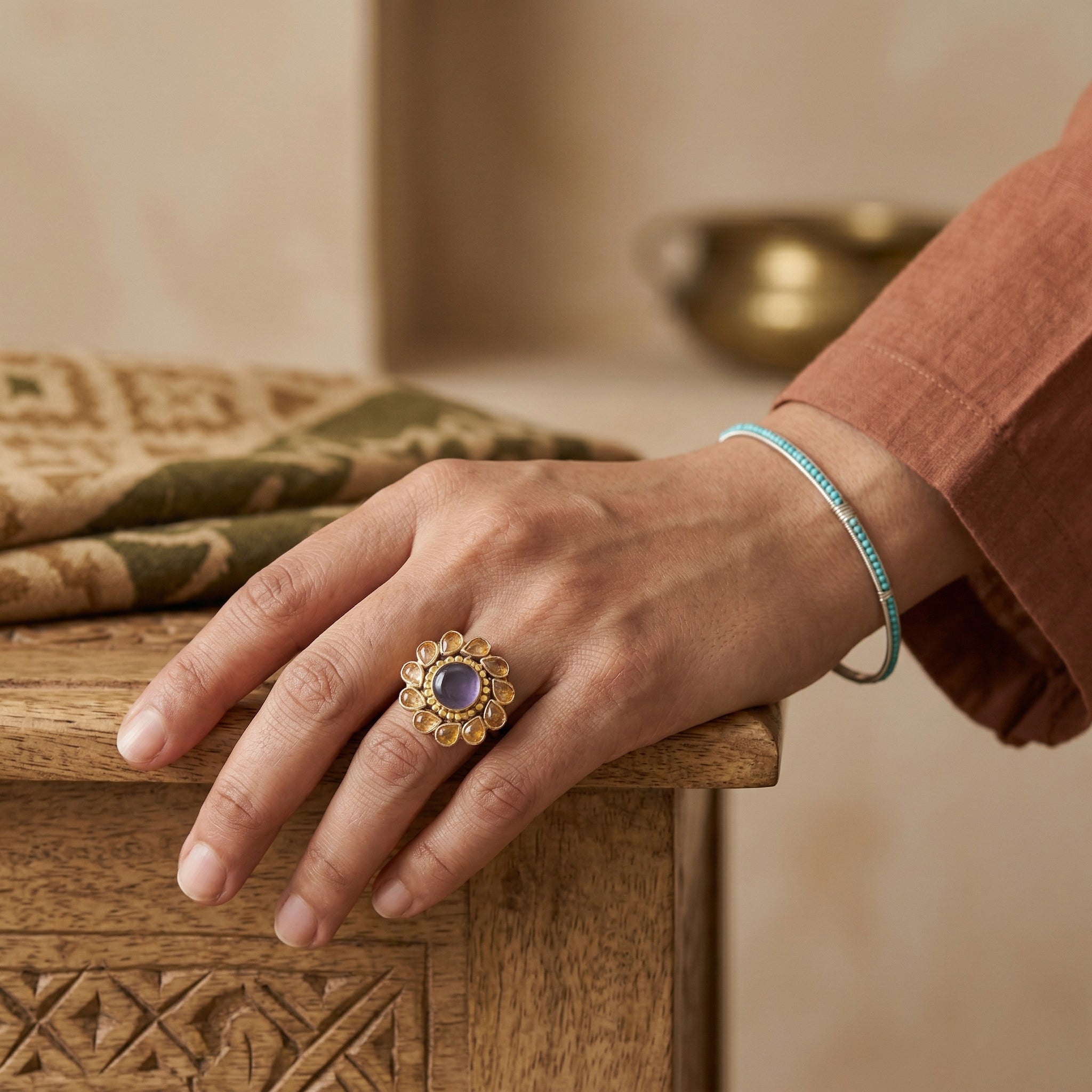 Hand wearing a gold ring with a purple gemstone on a wooden surface.