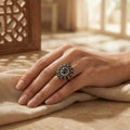 Hand wearing a decorative ring on a textured surface with a warm, blurred background