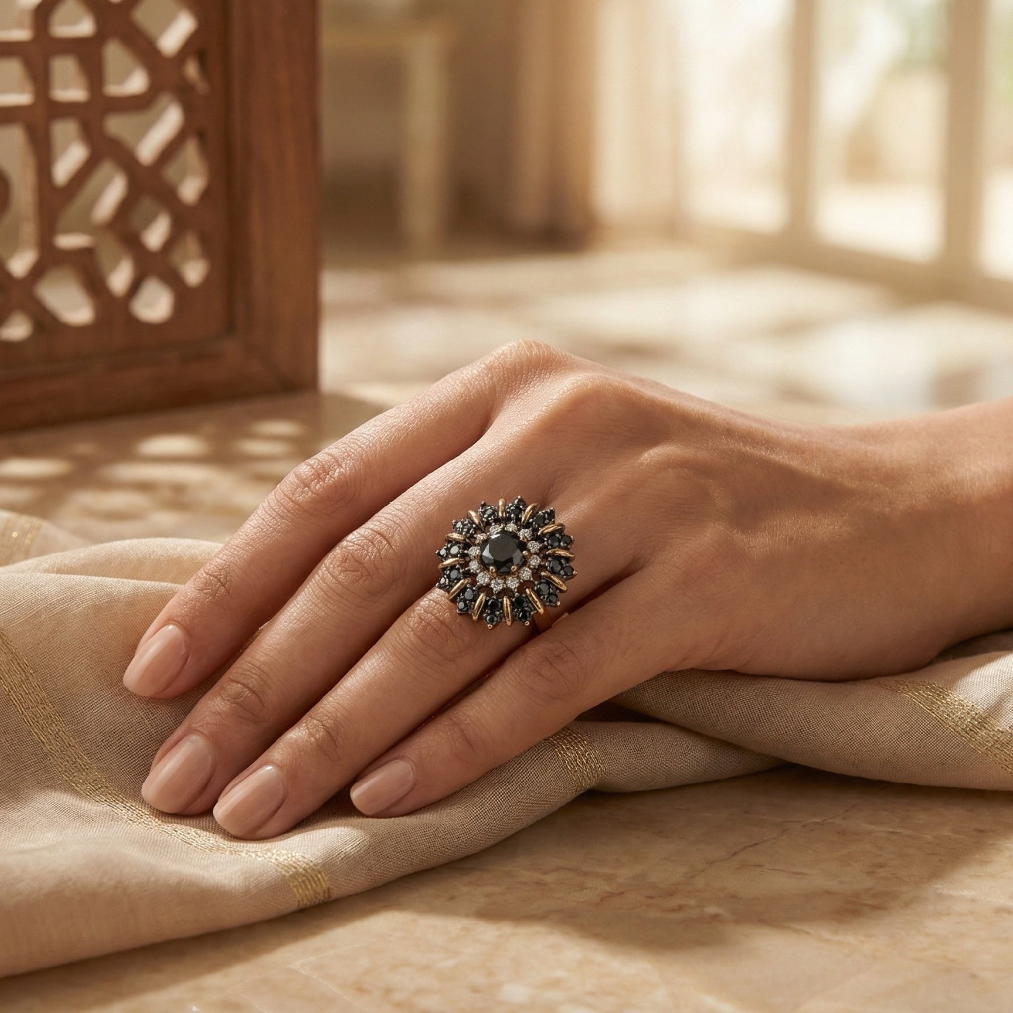 Hand wearing a decorative ring on a textured surface with a warm, blurred background