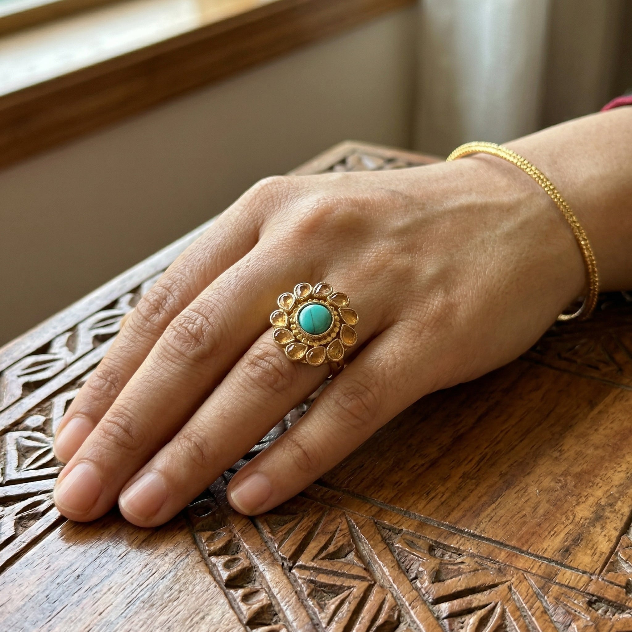 Hand wearing a gold ring with a turquoise stone on a wooden surface