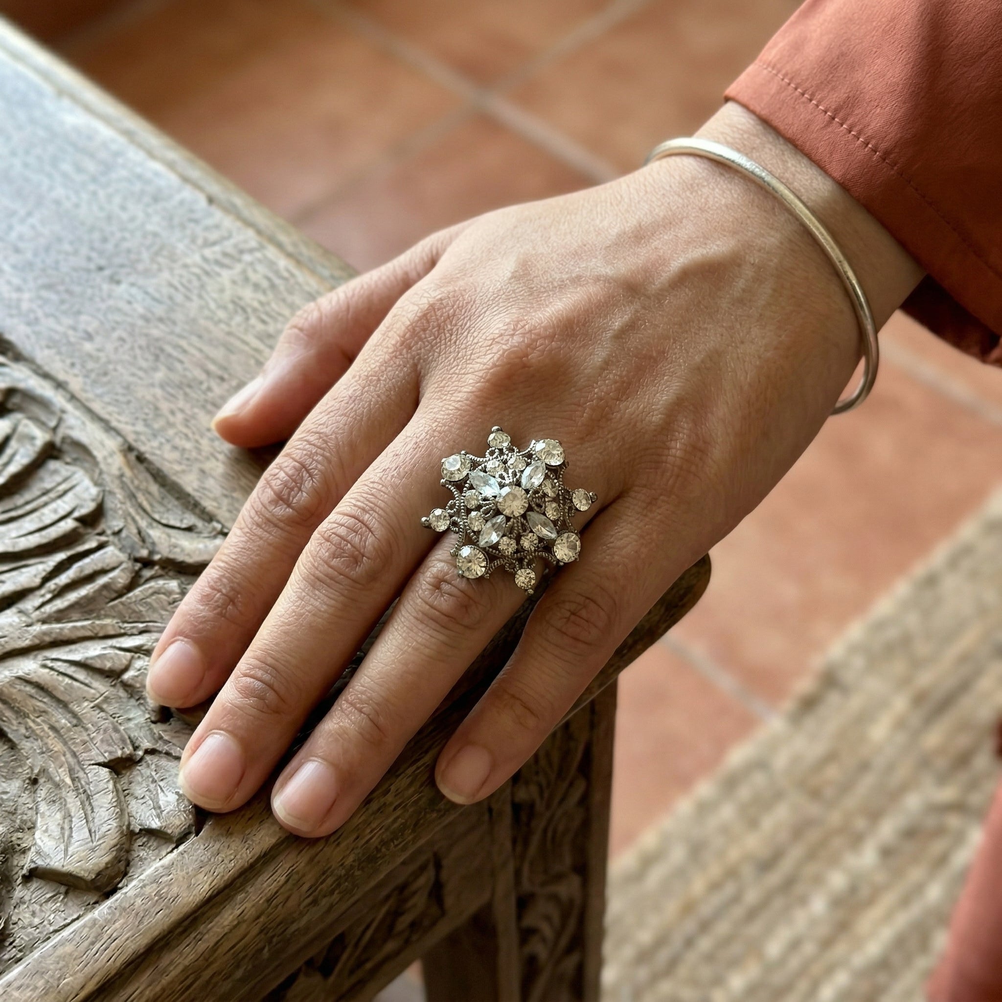 Hand wearing a decorative ring on a wooden surface