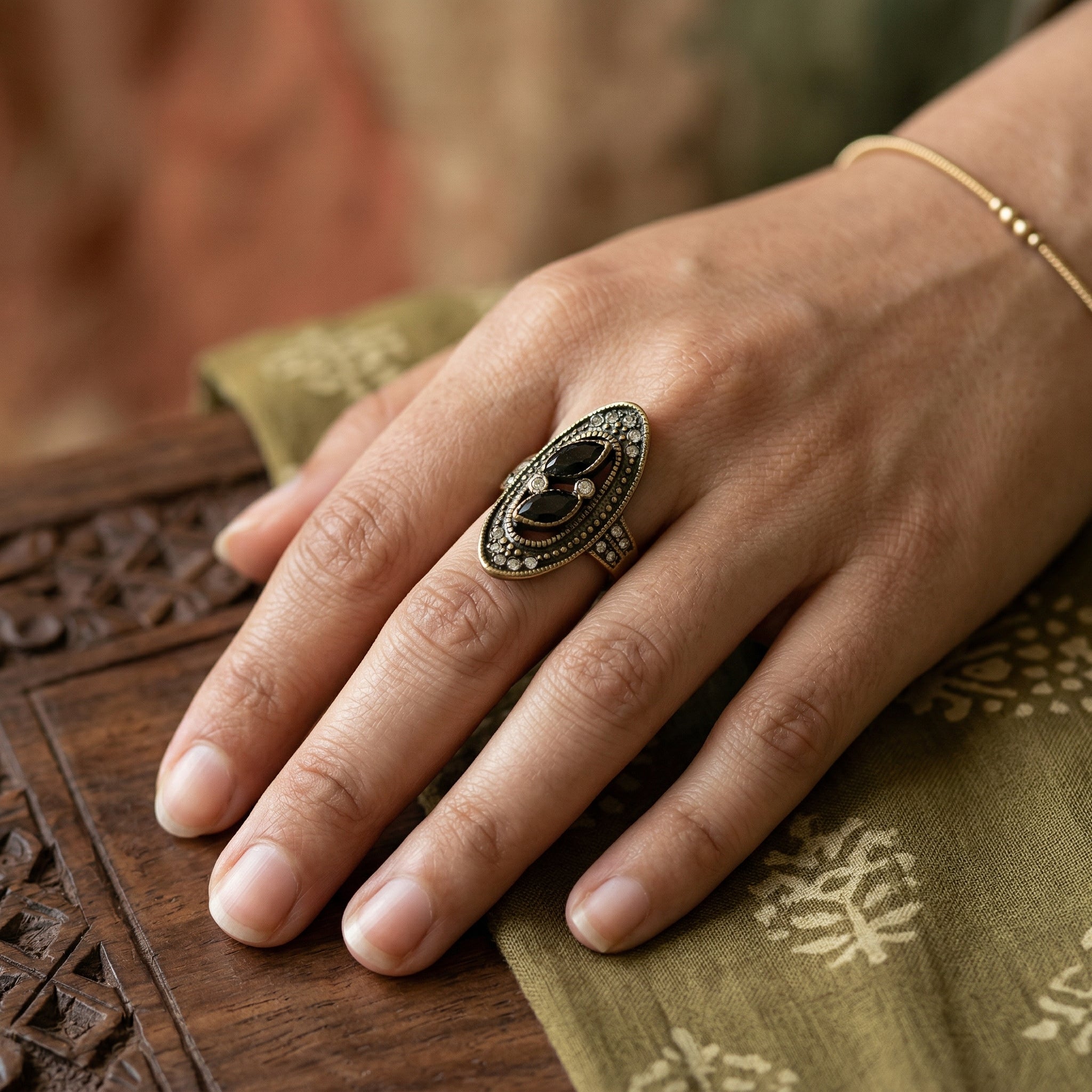 Hand wearing a decorative ring on a wooden surface with a blurred background