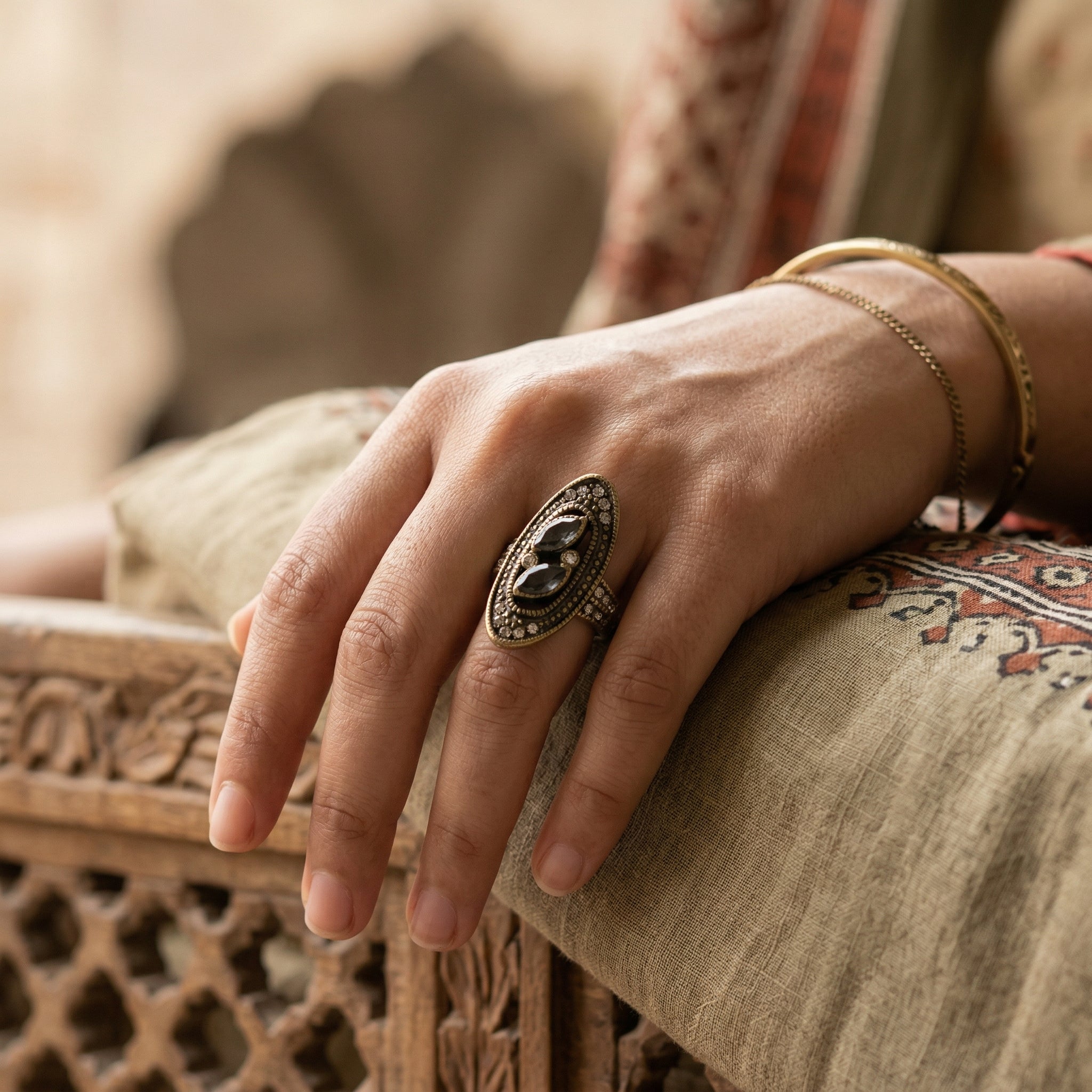 Close-up of a hand wearing an ornate ring on a patterned fabric background