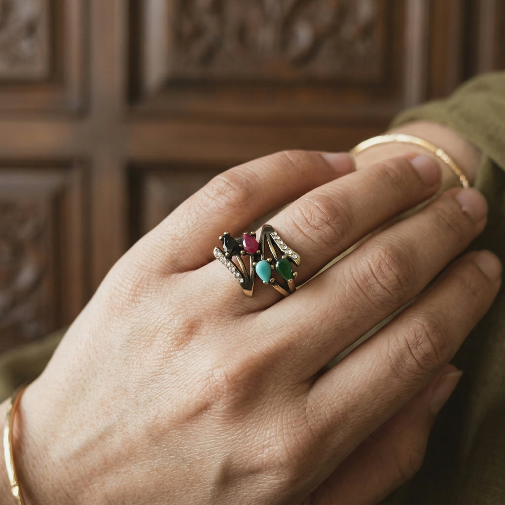 Hand wearing a ring with colorful gemstones against a wooden background
