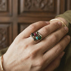 Hand wearing a ring with colorful gemstones against a wooden background