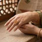 Close-up of a hand wearing a gold ring with intricate design on a textured surface.