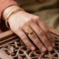 Hand wearing a gold ring on a wooden surface