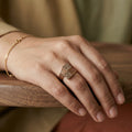 Hand wearing a gold ring and bracelet on a wooden surface