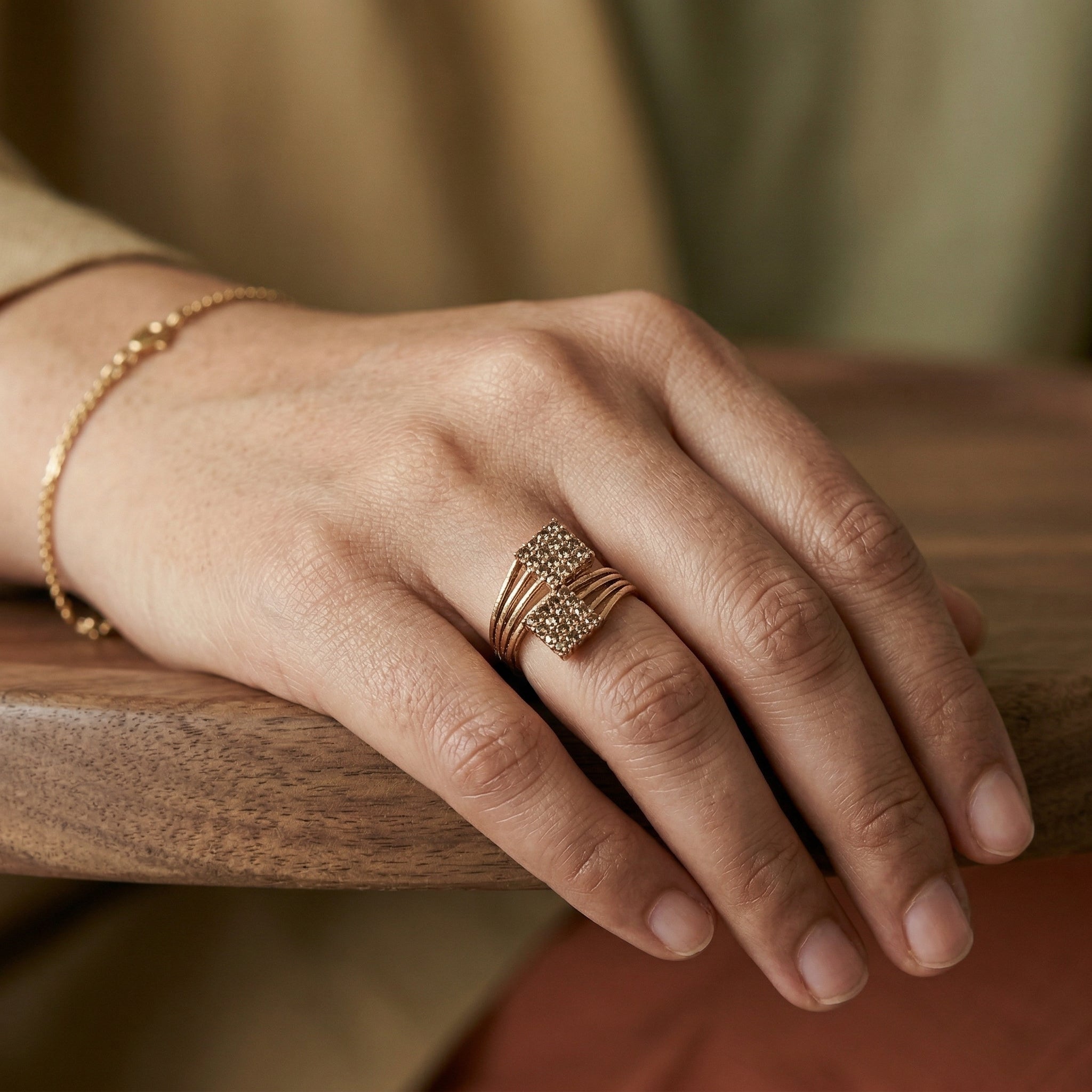 Hand wearing a gold ring and bracelet on a wooden surface