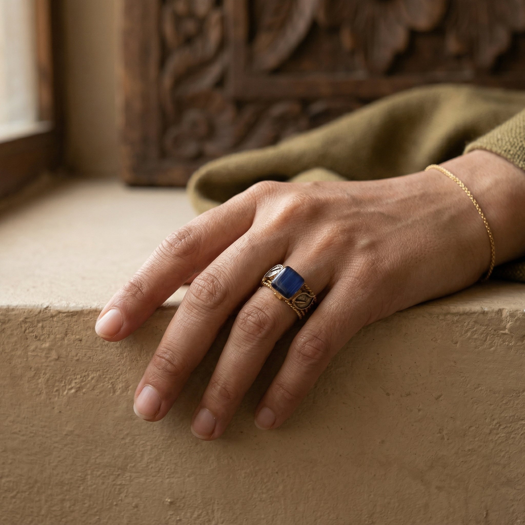 Hand wearing a gold ring with a blue stone on a textured surface
