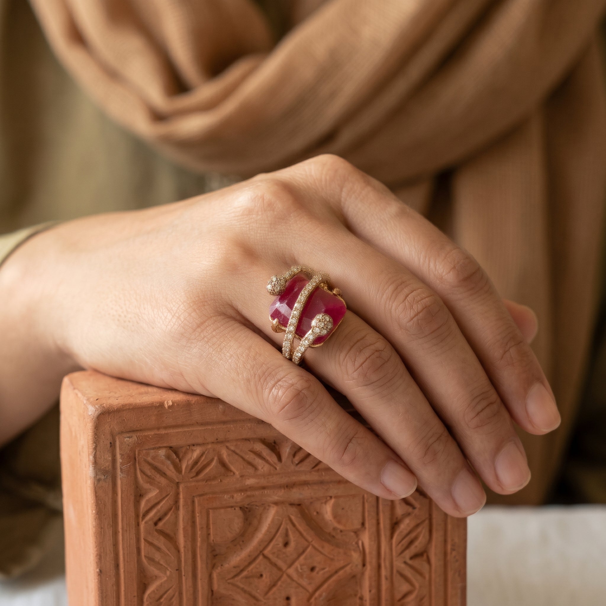 Hand wearing a ring with a red gemstone on a textured surface
