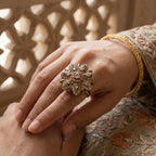 Close-up of a hand wearing a decorative ring with intricate design, against a blurred background.
